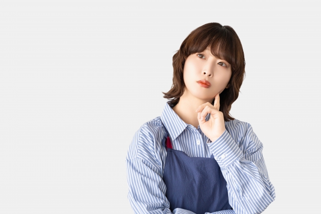 考えごとをするエプロン姿の女性