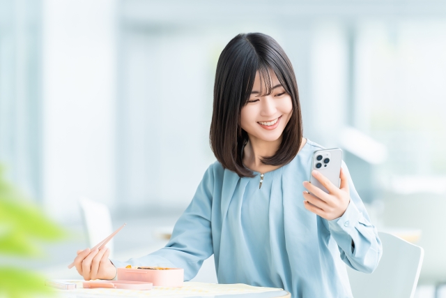 スマホを見ながらお弁当を食べる女性