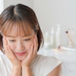 頬を押さえる女性と化粧品