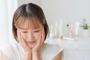 頬を押さえる女性と化粧品